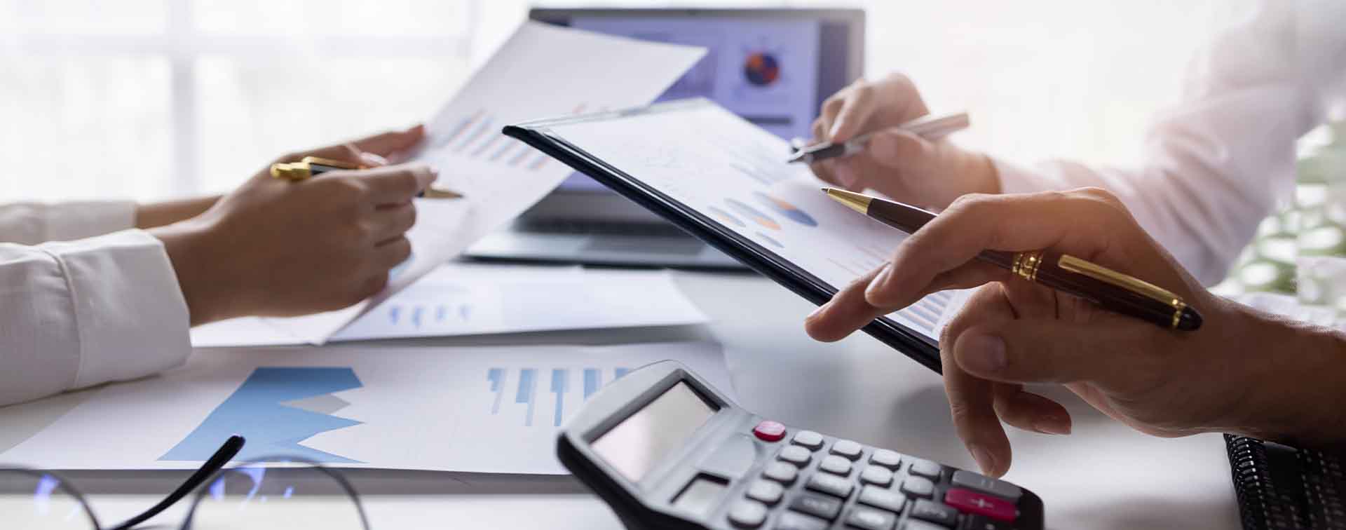 Close-up of financial experts analyzing charts as one types on a calculator