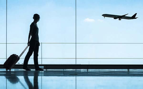Woman dragging a suitcase looking out of a window at a plane taking off