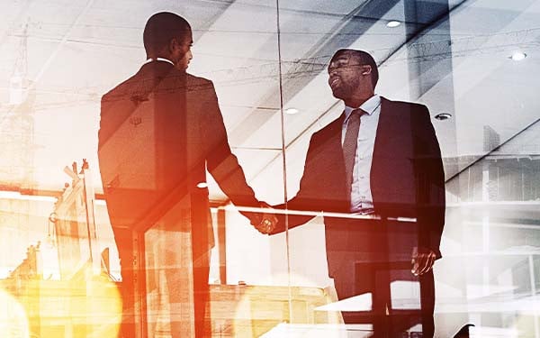 Glass building shot of wwo men shaking hands at sunset.