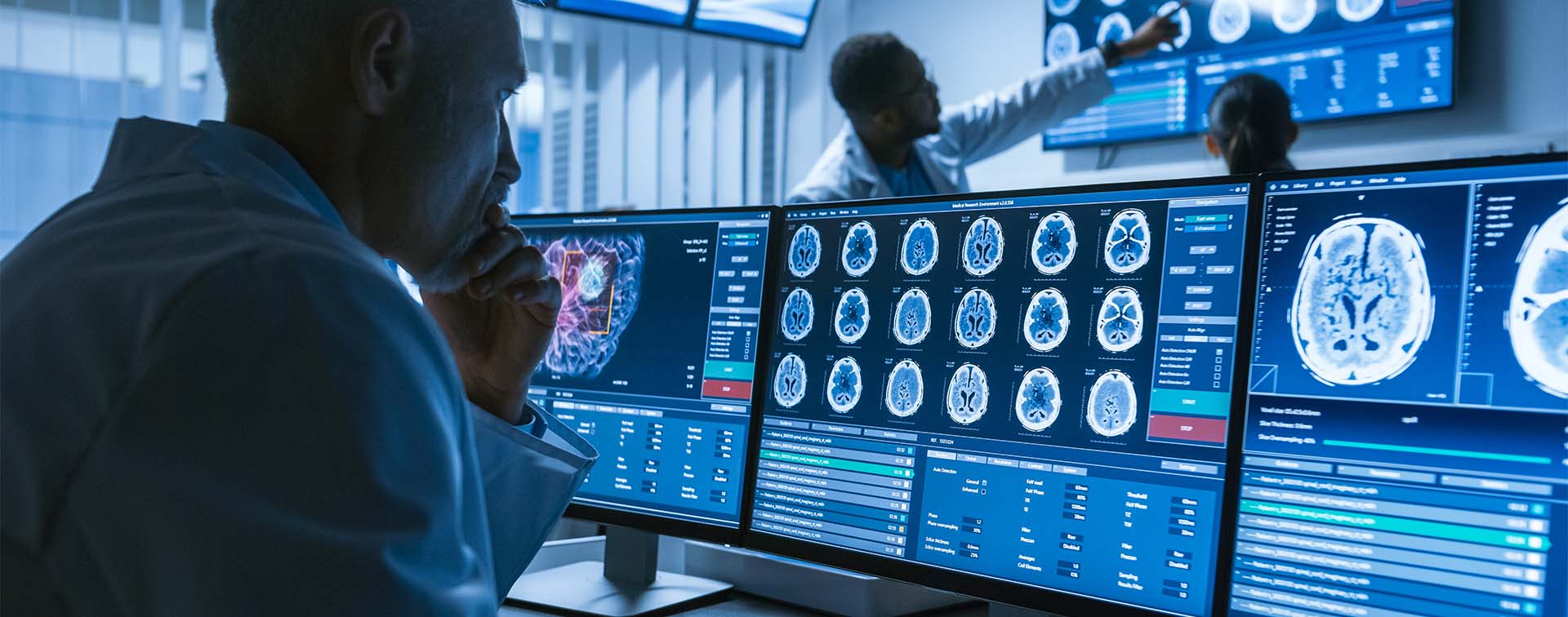 Over-the-shoulder shot of medical scientist and neurologists looking at CT brain scans on laboratory computers