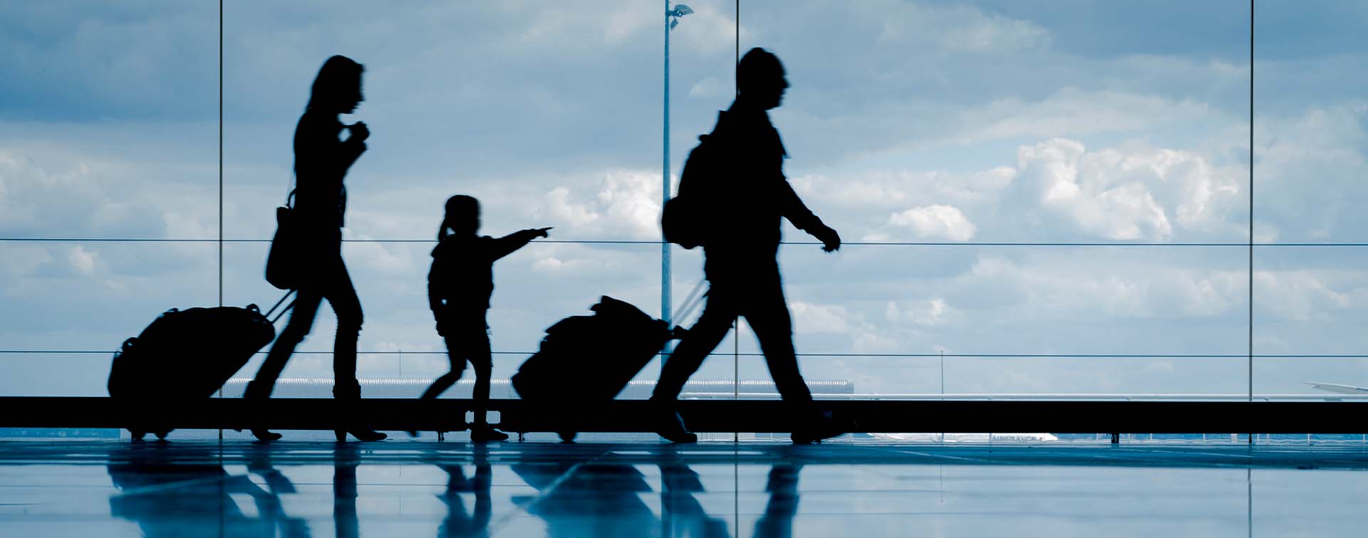 Silhouette of young family with luggage walking at airport, girl pointing at the window